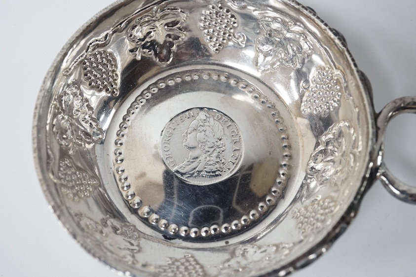 A George V silver taste vin, by Daniel & John Welby, with fruiting vine decoration and inset coin centre, London, 1924, diameter 92mm, 4.1oz. Condition - fair to good